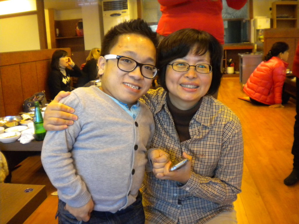 A young male adult adoptee and physical therapist smile for the camera