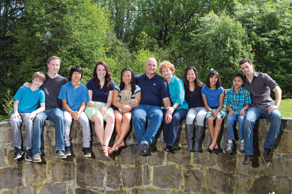 The Henderson clan. From left: Sam, Tyler, Alex, Emily, Grace, Clay, Shila, Qiulan, Anna, Luke and Jordan. The teddy bear belonged to Shila and Clay’s son Drew, who passed away from cancer in 2007.