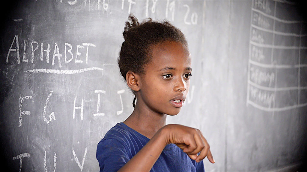 A girl practices signing the English alphabet in front of her classmates.