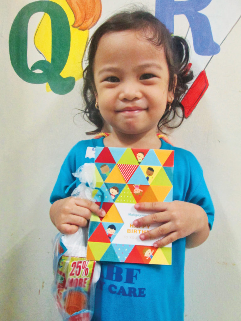 Ada Belle - a child in Holt's child sponsorship program - holding up a birthday card and gift