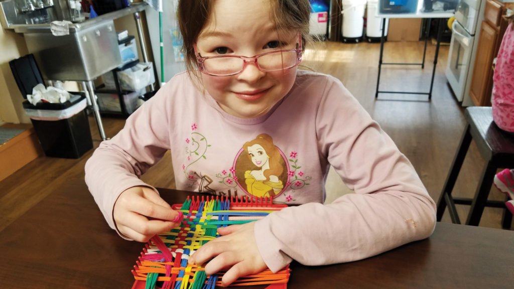 Madison using a loom to create the colorful potholders she sells to buy holiday gifts for Hui, her family's sponsored child..