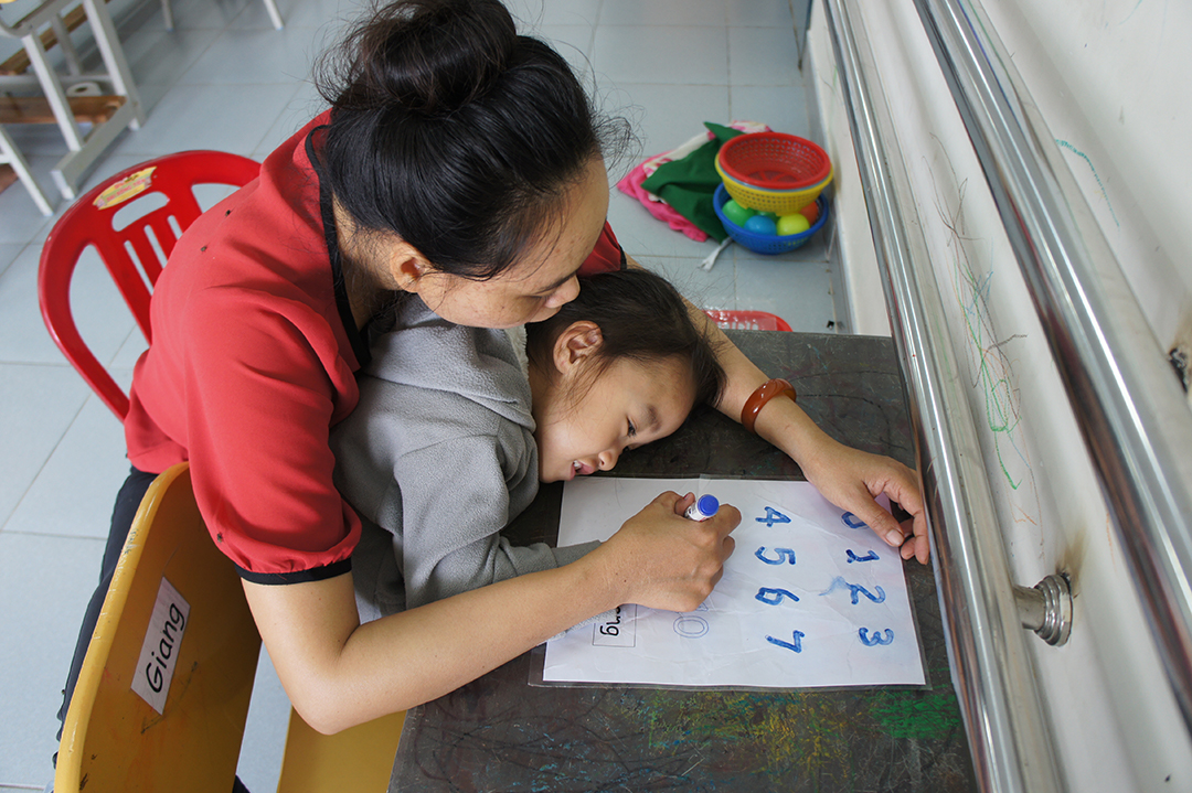A teacher working with Giang on writing numbers at Kianh Foundation — a school and day care center specifically for children with special needs.