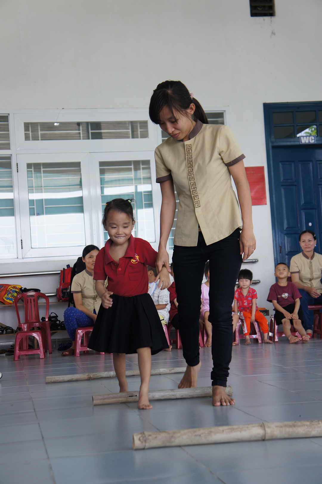 A teacher helping Giang walk over logs