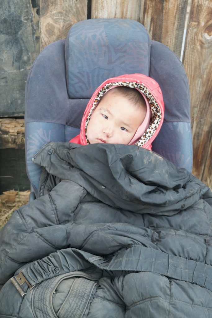 Amin-Erdene's cousin sits in an old car seat on the property outside their gers.