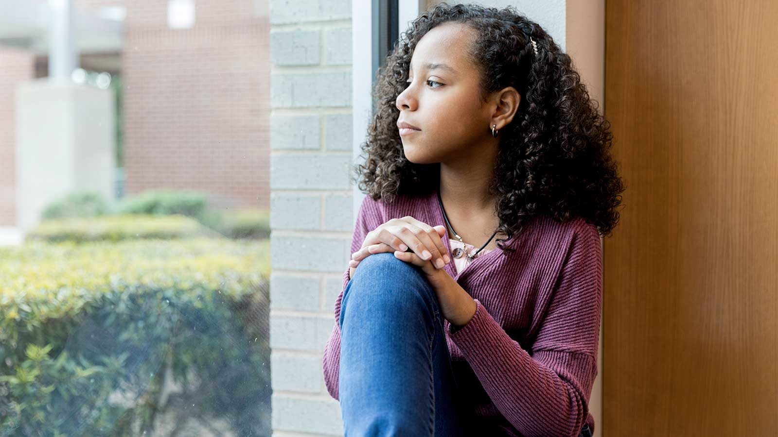 Preteen girl looking out the window with serious expression