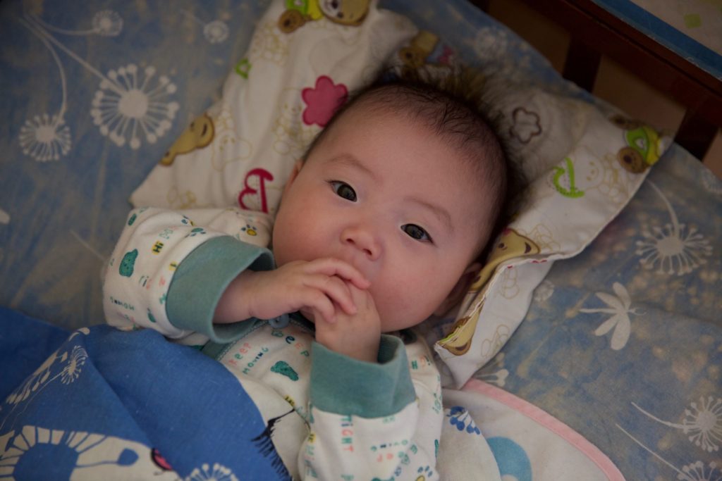 Photo of baby lying in crib with hands in mouth