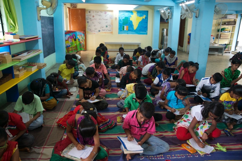 Children at the DEESHA write personal essays during camp. Raji is in the second row from the right, seated five children from the front.