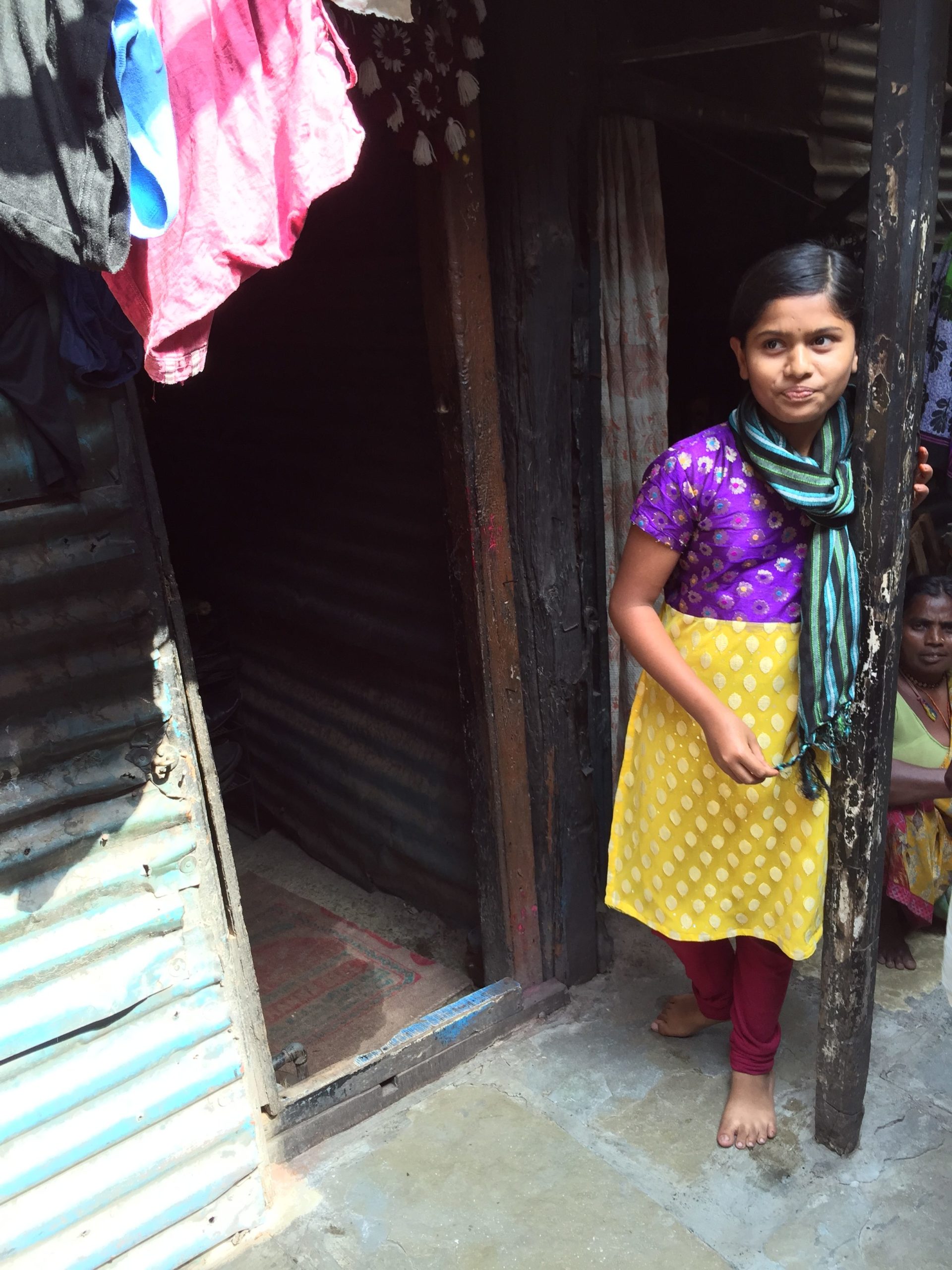 Raji, 12, stands outside the door to her home.