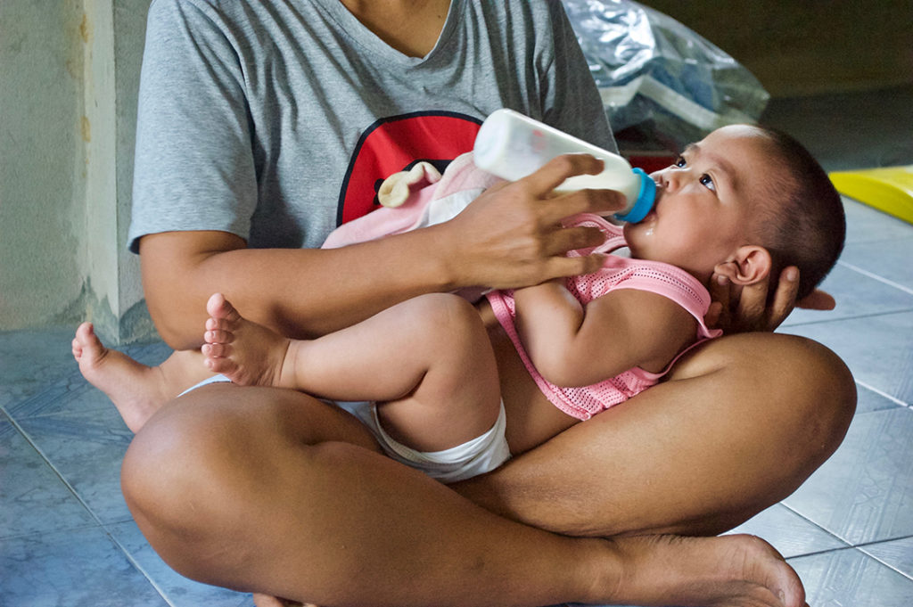 Ping feeding one of her twin babies with a bottle. Without support from child sponsorship she would have to feed her sons sweetened condensed milk instead of infant formula.