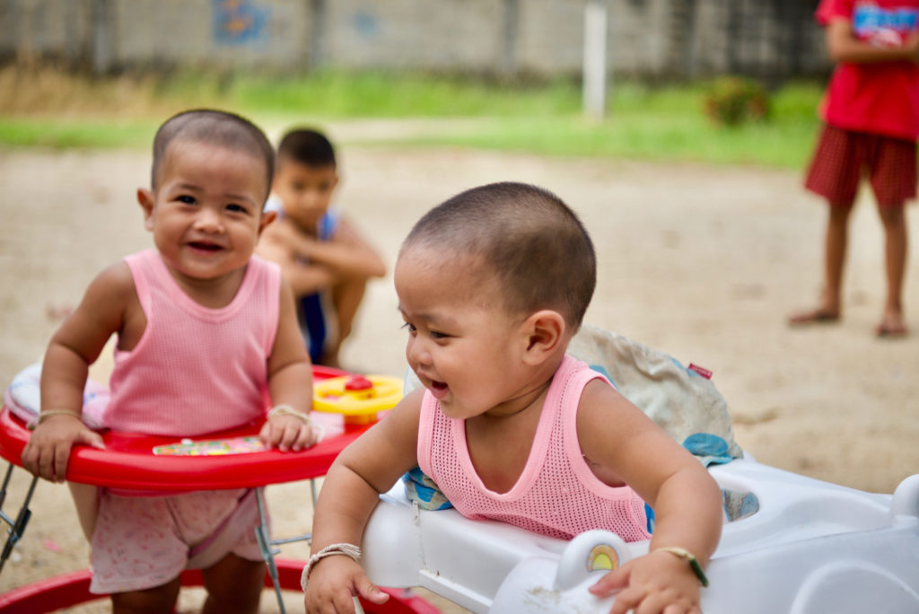 Ping's two babies in walkers smiling.