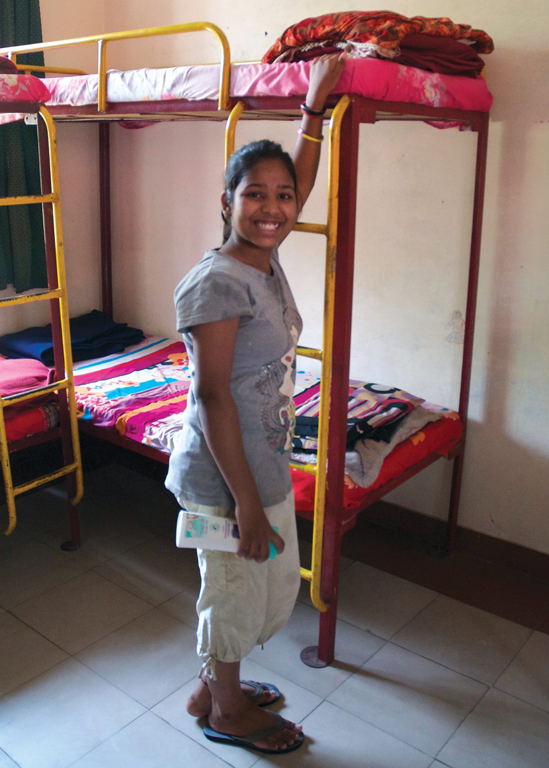 Sponsored girl and a hostel resident stands by her bunk bed.