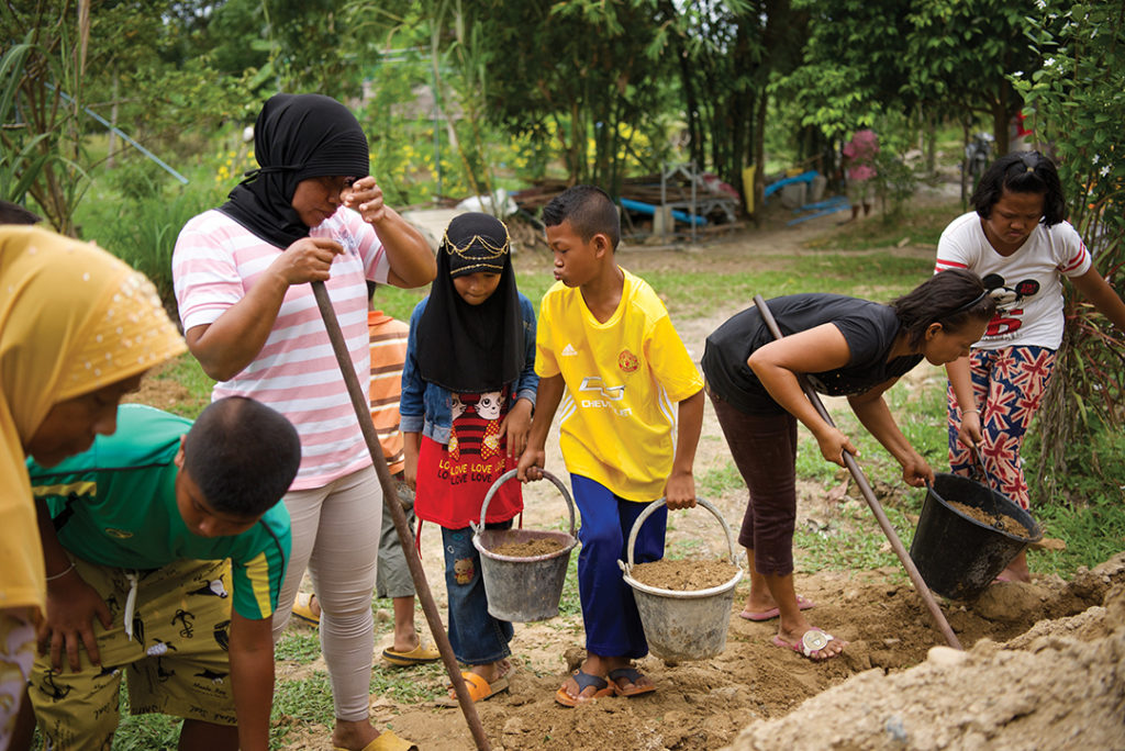 group of adults and children carrying buckets of dirt
