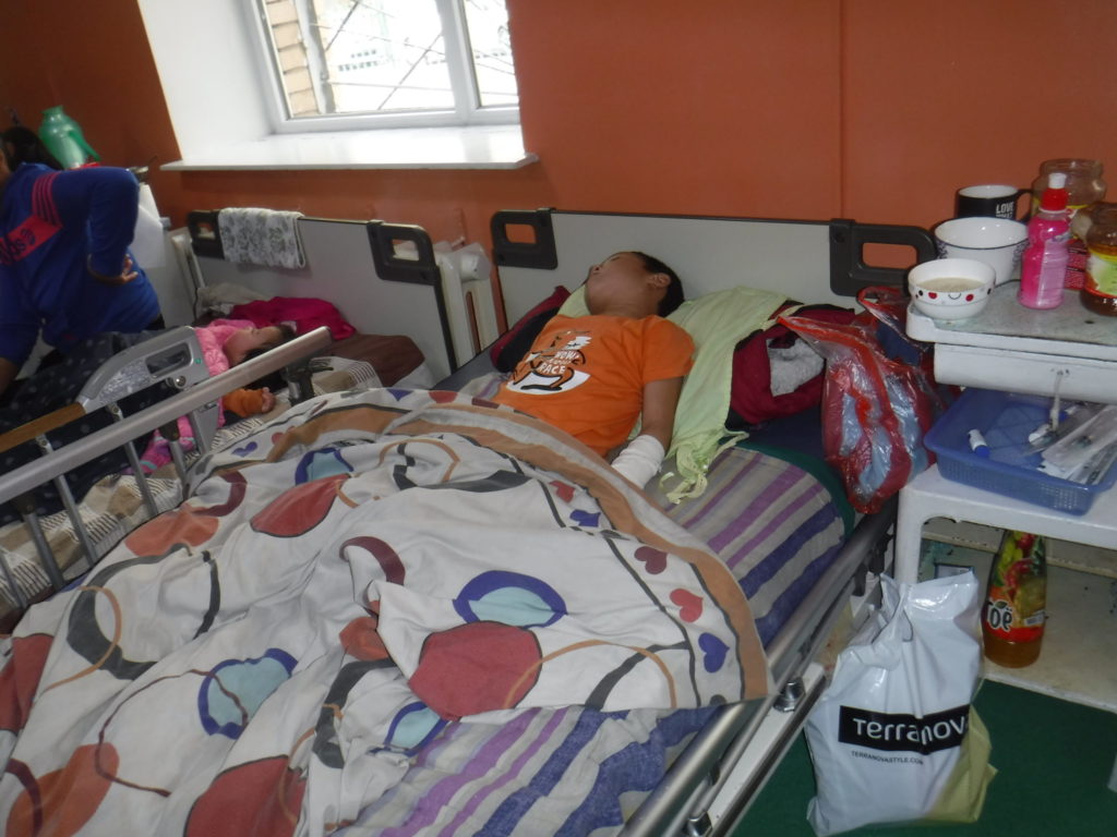 After falling on his family's stove in the night, Munkh was hospitalized for significant burns on his hands and legs. Photo of Munkh lying in hospital bed.