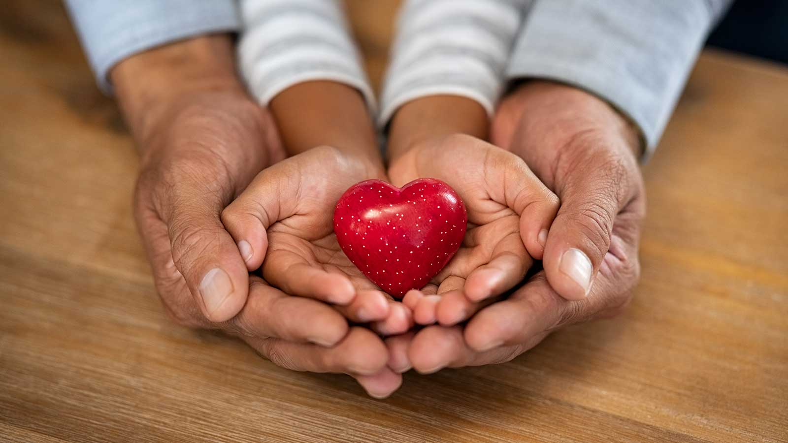 Adult hands holding child's hands holding a heart