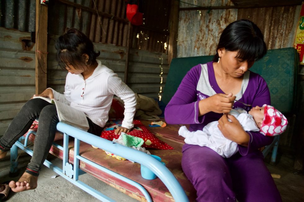 Linh reads while her mom feeds Linh's baby. 