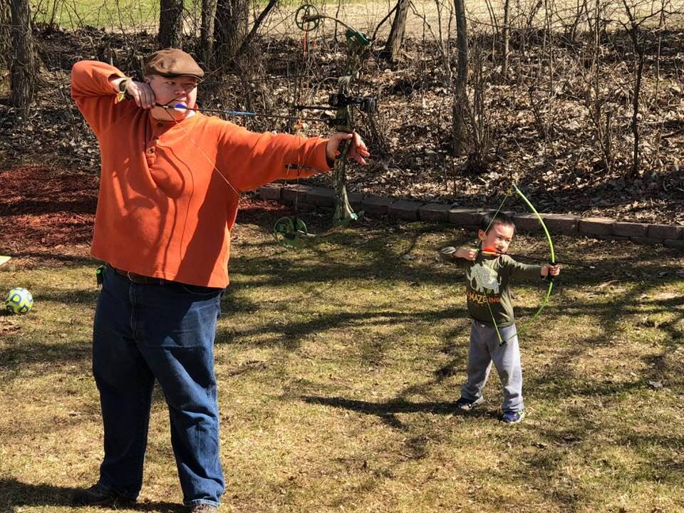 Adoptive father and son outdoors pulling back on a bow and arrow