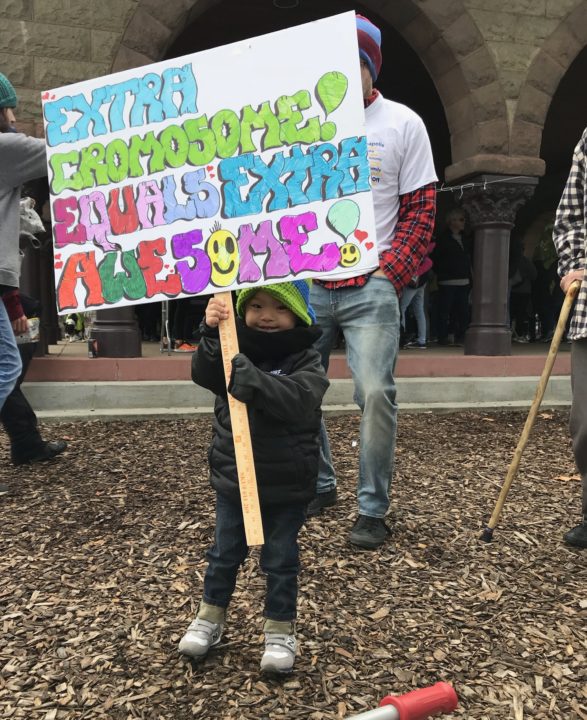 Micah holding a sign that says, "Extra chromosome! Equals extra awesome!"