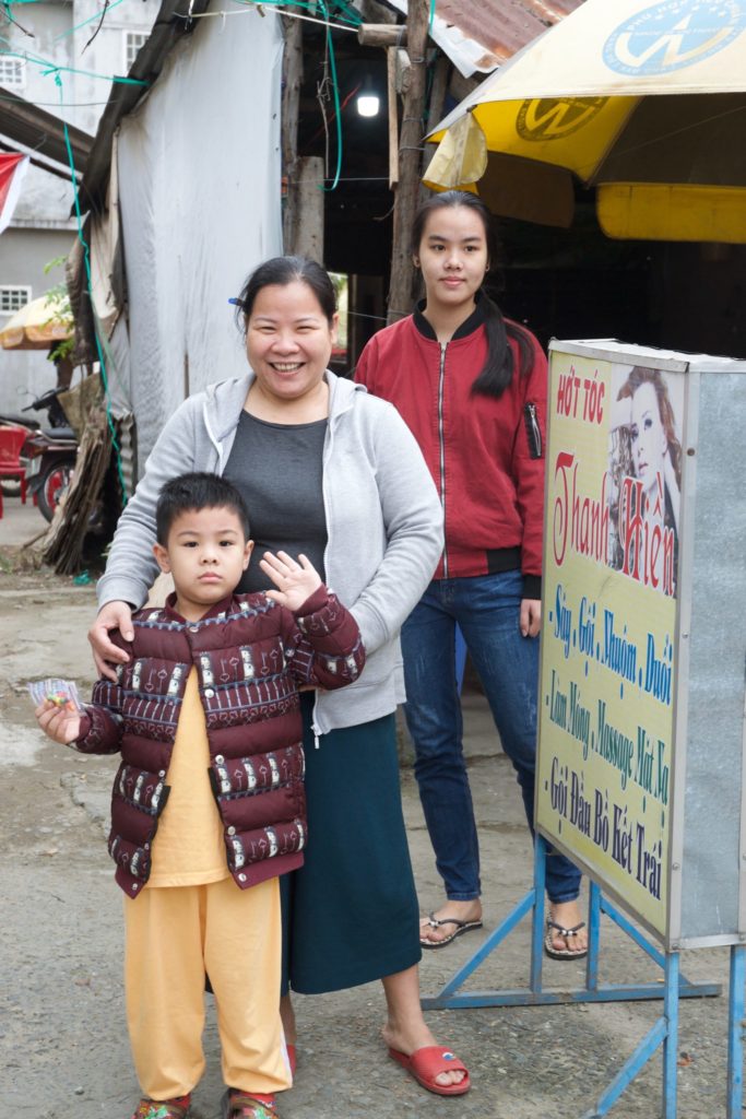 Vieng, Hung and Hung's oldest sister stand beside the sign for their salon business.