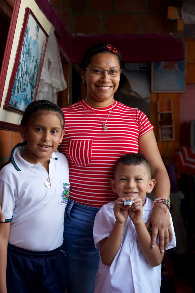 Mary Luz smiling and standing with her arms around both of her children.