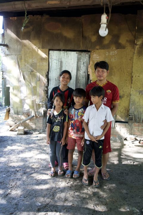 Thak Kan and his family stand in front of their old house, which had holes in the walls and floor that let in snakes and scorpions. 
