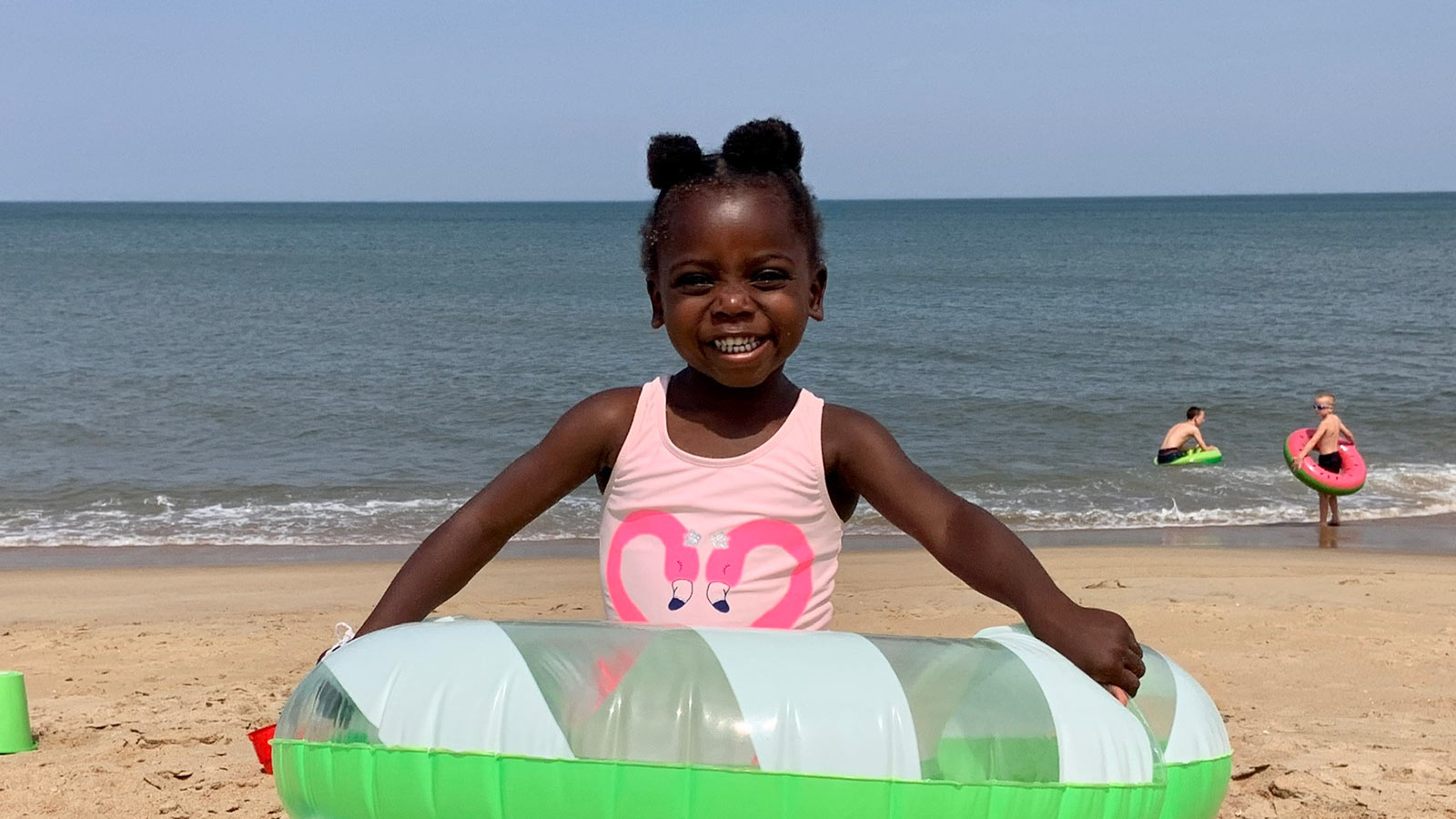 smiling girl adopted from Haiti wearing flamingo swimsuit and green inner tube at the beach