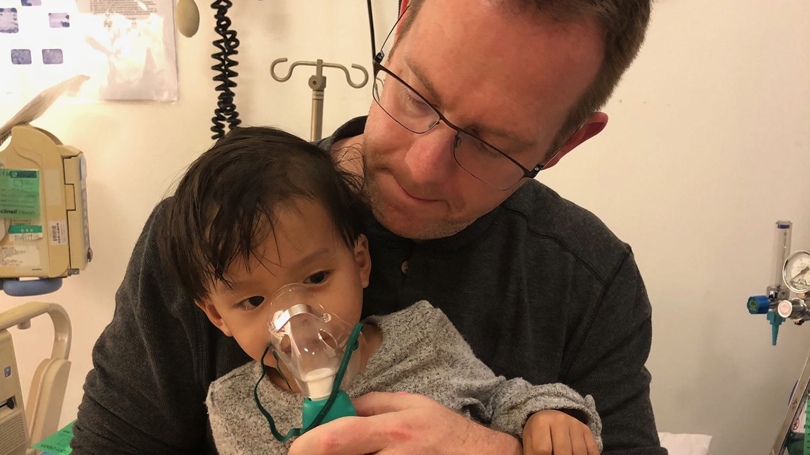 man holding small baby wearing oxygen mask