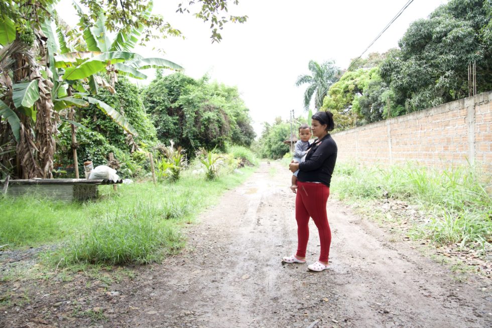 Diana holds her son as she stands in the road that divides her community from the wealthy landowners who live behind the wall.