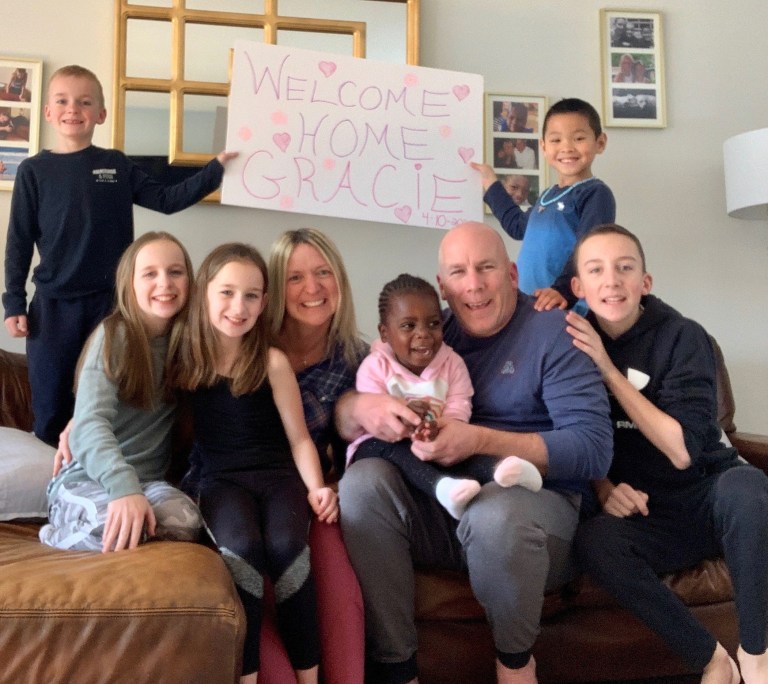 family sitting on couch with sign that says "welcome home gracie"