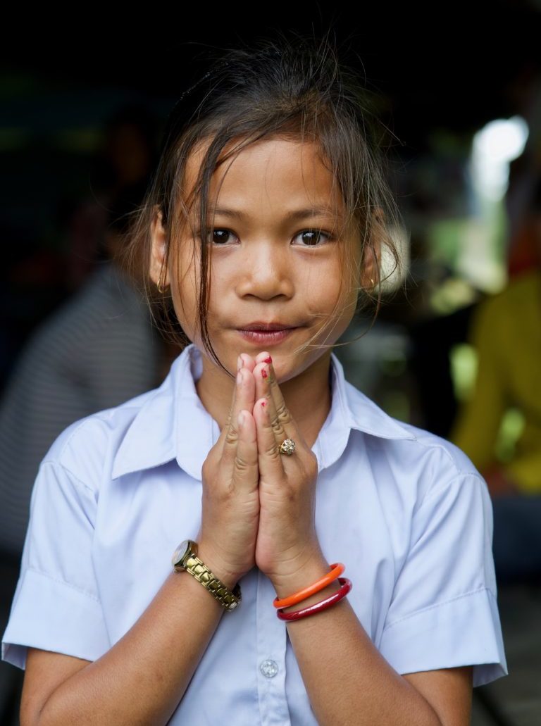 Sponsored girl in Cambodia holding hands in prayer, sampeah, in school uniform