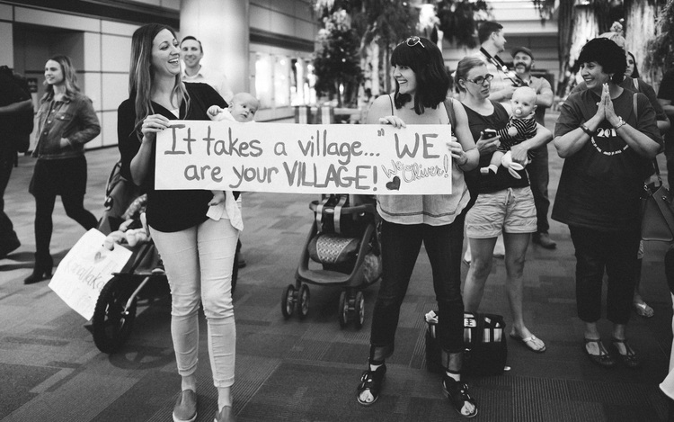 women holding a sign that says "it takes a village...we are your village!"