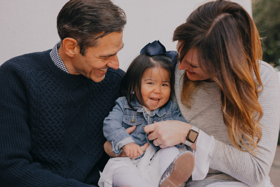 dad and mom looking down and smiling at laughing girl