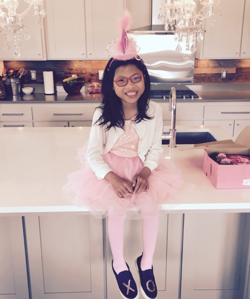 little girl in birthday hat sitting on kitchen counter