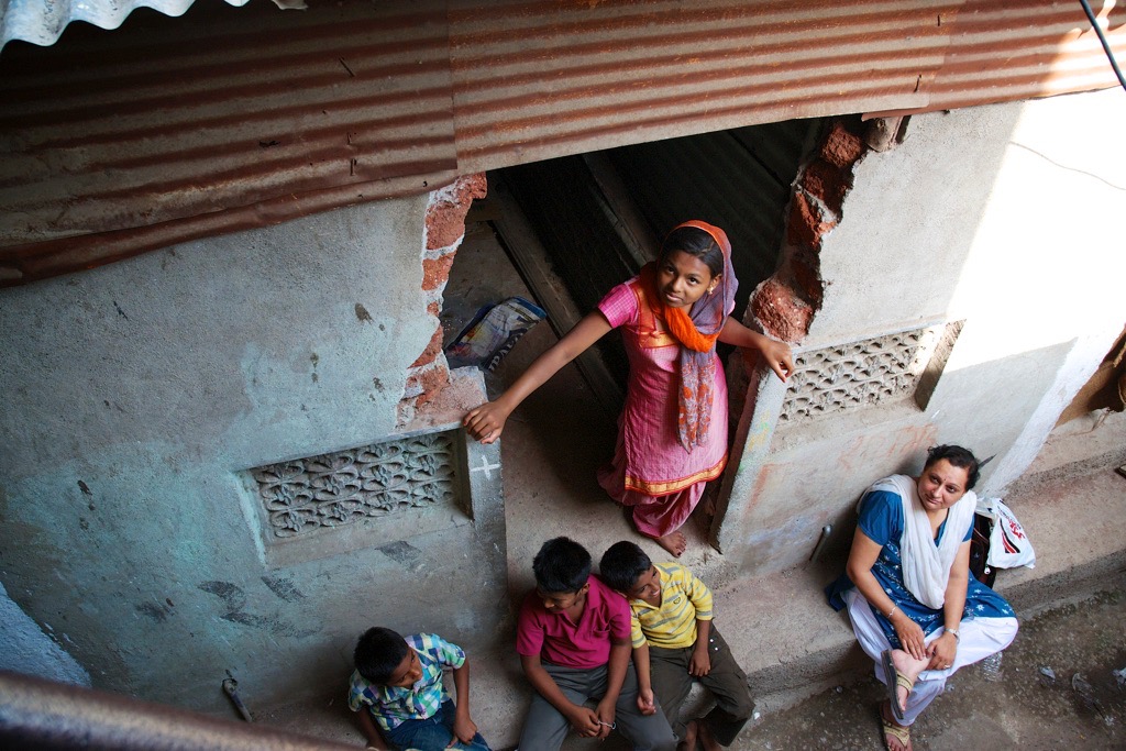 girl standing in doorway of slum home looking up at camera