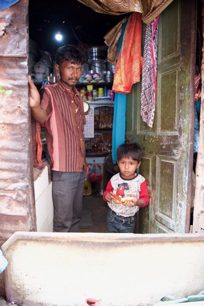 father and little boy standing in doorway of slum home in India