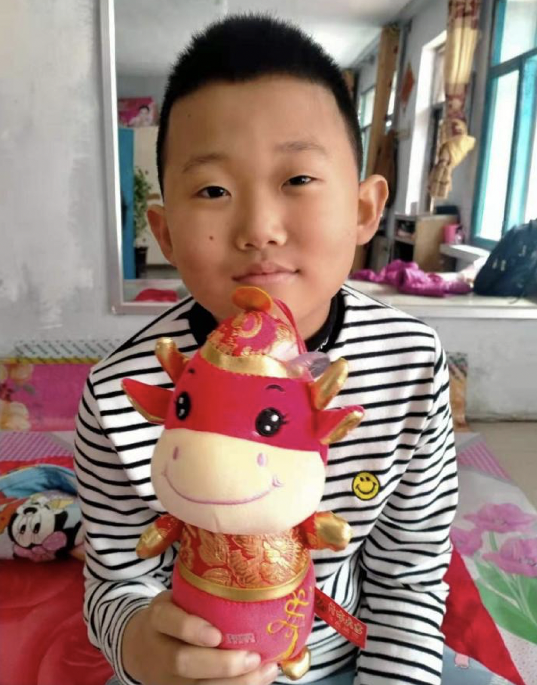 smiling boy in China holding stuffed ox recovering from heart surgery