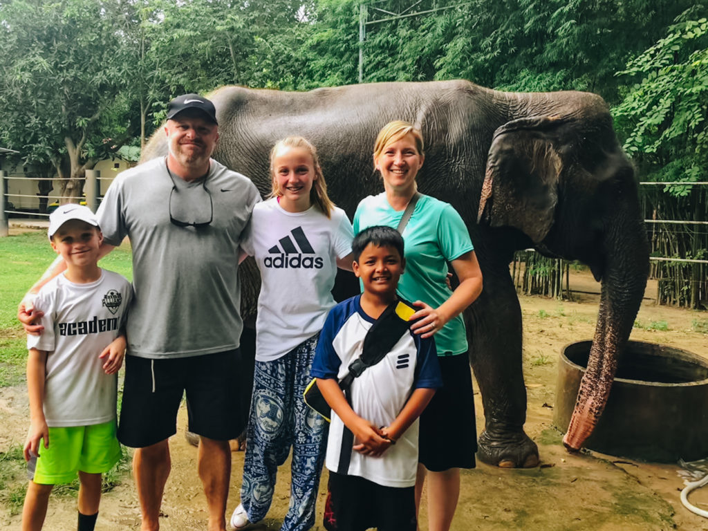 family of five standing in front of elephant