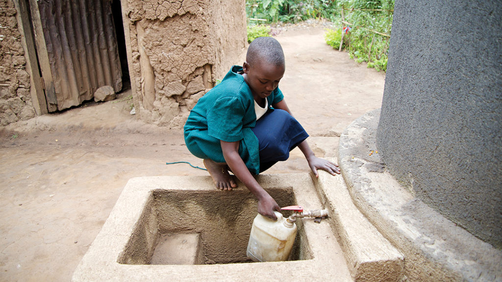 girl kneeling to fill jug of water