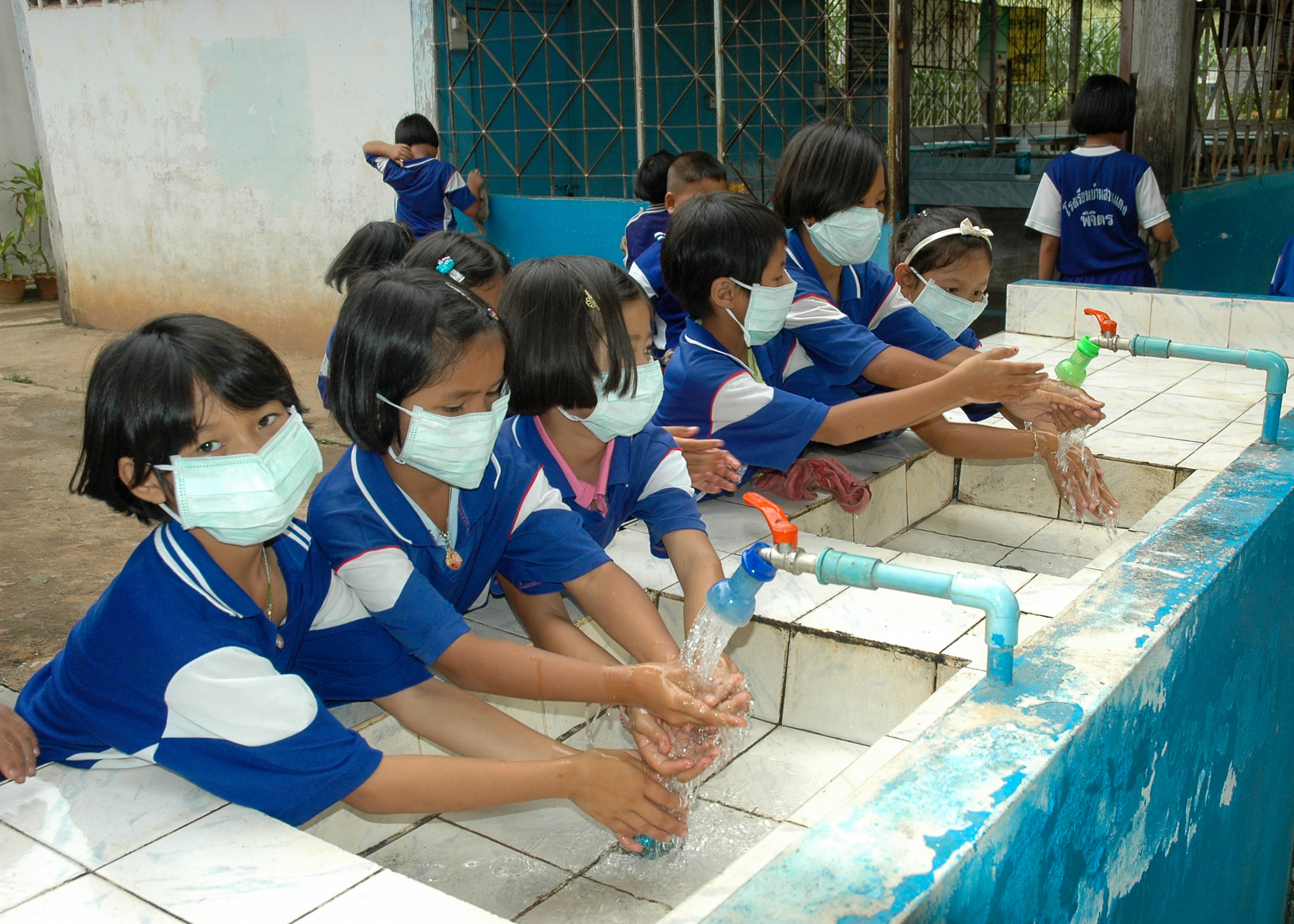 group of children in uniforms and masks washing their hands