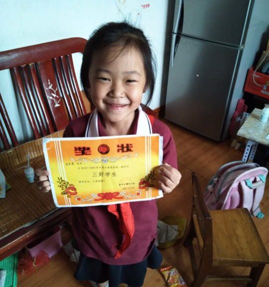 Seven-year-old Ju holds a certificate of achievement from her school. 