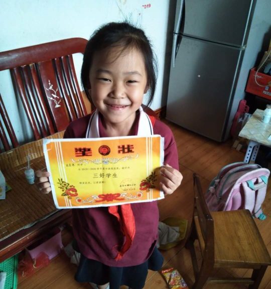 Seven-year-old Ju holds a certificate of achievement from her school.