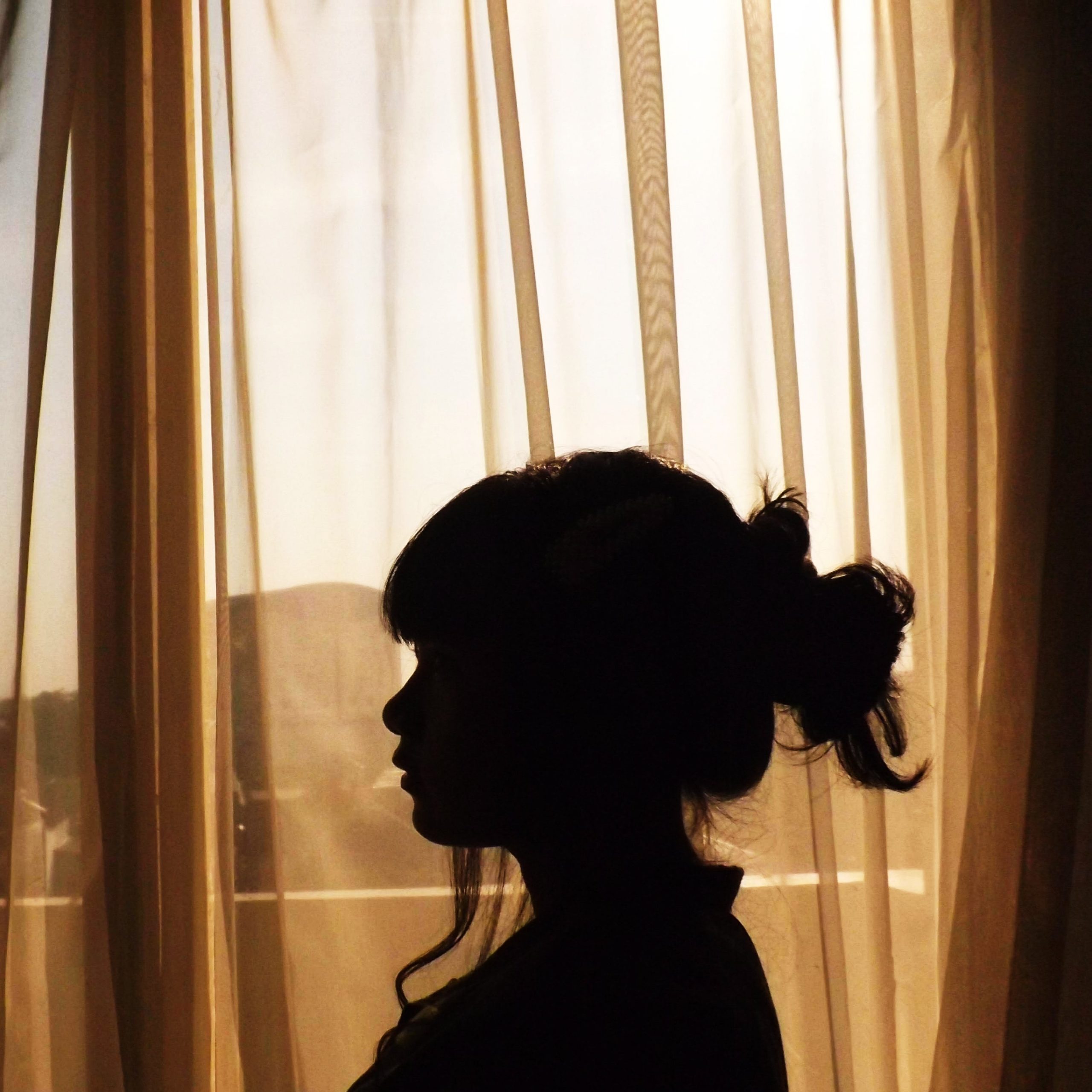 silhouette of woman with messy bun in front of sheer curtain