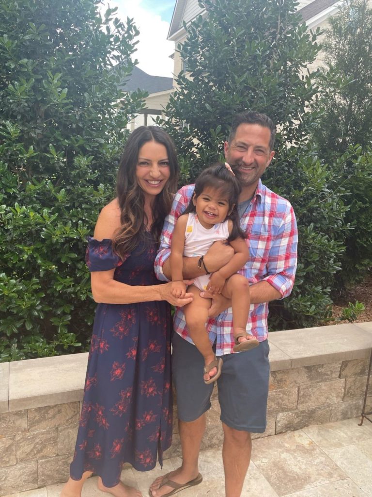 smiling woman next to smiling man holding toddler girl