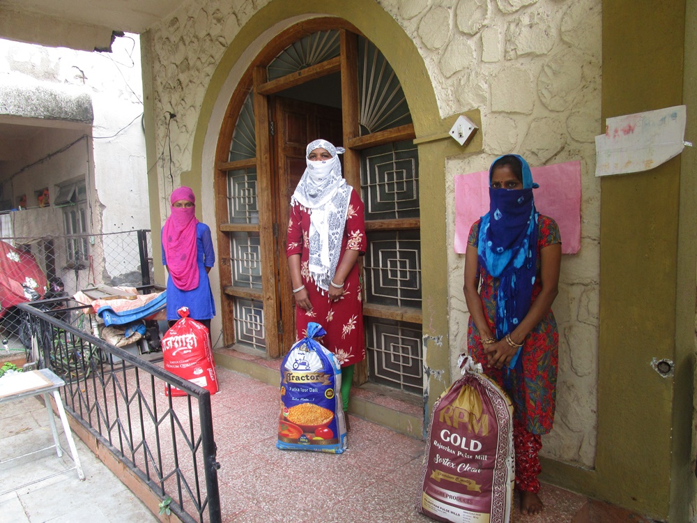 three women standing holding bags of grain