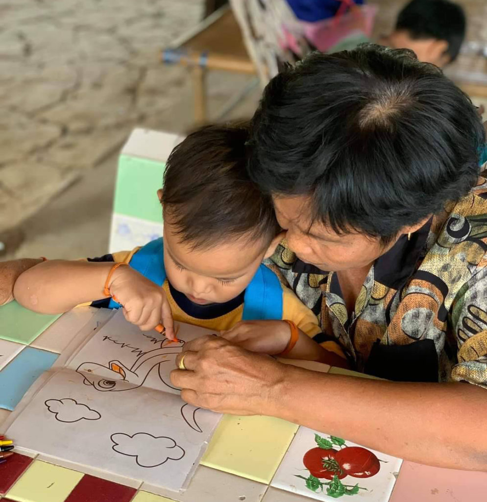 young boy coloring sitting in the lap of foster parent