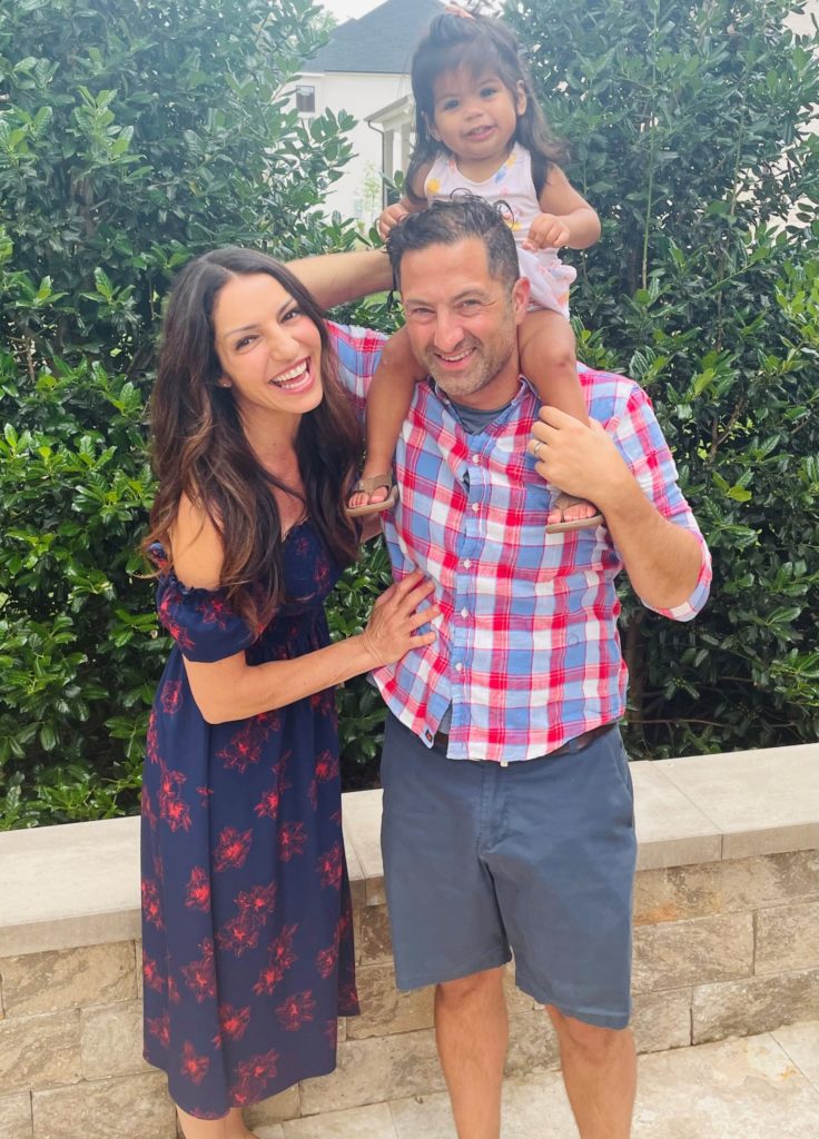 laughing woman next to smiling man with toddler girl on his shoulders