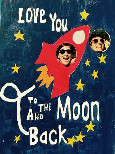 man and woman smiling by sign that says "love you to the moon and back"