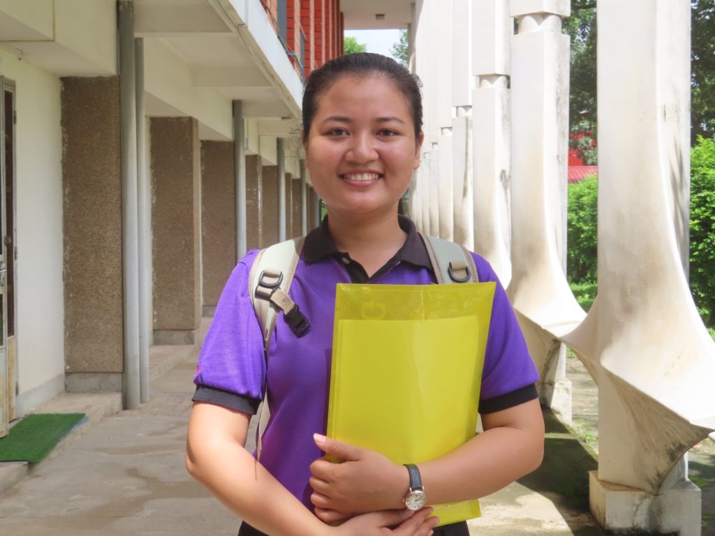 girl in purple polo holding yellow folder smiling at camera