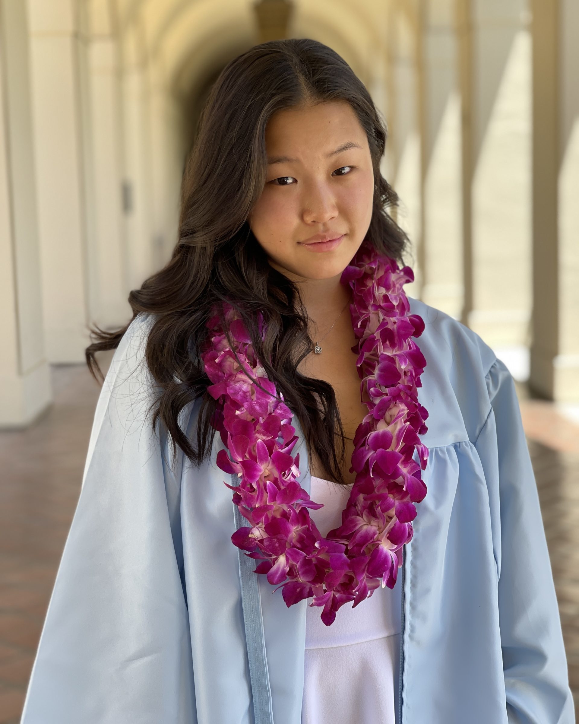 girl wearing light blue graduation gown and purple lei