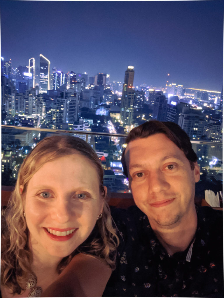 selfie of man and woman in front of night city skyline