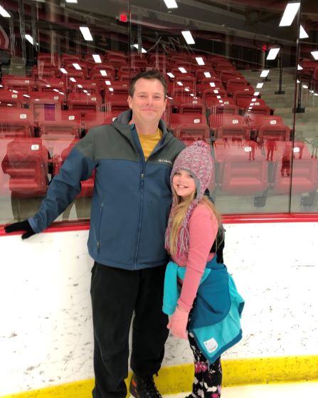 man with arm around daughter on ice rink